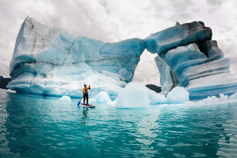 Man on paddle board in front of glacier