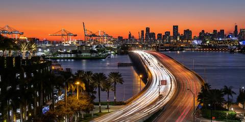 traffic moving over a bridge with cranes in the distance at dusk